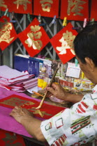 Thailand, Bangkok, Calligrapher painting Gold characters on red paper auspicious colours for Chinese New Year.