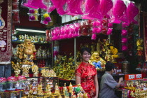 Thailand, Bangkok, Young woman in Cheong sam chinese dress at shop selling decorations for Chinese New Year.