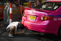 Thailand, Bangkok, Pink metered taxi cab being refuelled with LPG gas pipe.