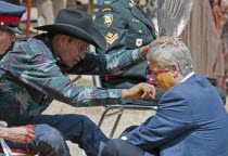 Canada, Alberta, Stand Off, Canada's Prime Minister, Stephen Harper, seated on a buffalo skin rug as Medicine Man Pete Standing Alone applies paint to his face as part of the ceremony to induct him in...