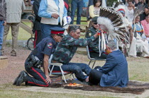 Canada, Alberta, Stand Off, Canada's Prime Minister, Stephen Harper, seated on a buffalo skin rug as Medicine Man Pete Standing Alone places a ceremonial  headdress of Eagle feathers on his head as pa...