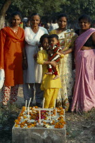 India, Delhi, All Souls Day in Christian cemetary, family group around grave decorated with flowers and candles.