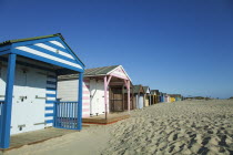 England, West Sussex, West Wittering Beach, Colourful beach huts along sandy beach.