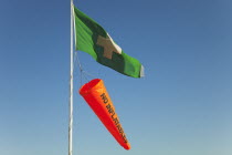 England, West Sussex, West Wittering Beach, Beach safety flags. White Cross on Green Flag signalling First Aid Point. Orange No Inflatables windsock.