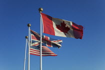 England, West Sussex, West Wittering Beach, Canadian , British and United States of America flags flying against a blue sky.