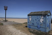 England, Kent, Romney Marsh, Littlestone Beach, Hut painted with Seahorse design and seafront torch beacon.