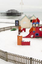 England, East Sussex, Brighton, West Pier during winter with snow on the beach and childrens play area in the foreground.