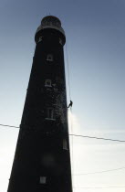 England, Kent, Romney Marsh, Dungeness, Man cleaning Lighthouse tower with pressure washer whilst abseiling.