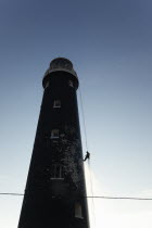 England, Kent, Romney Marsh, Dungeness, Man cleaning Lighthouse tower with pressure washer whilst abseiling.