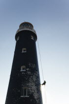 England, Kent, Romney Marsh, Dungeness, Man cleaning Lighthouse tower with pressure washer whilst abseiling.