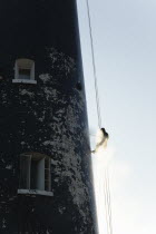 England, Kent, Romney Marsh, Dungeness, Man cleaning Lighthouse tower with pressure washer whilst abseiling.