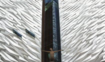 Ireland, North, Belfast, Titanic Quarter, Visitor centre designed by Civic Arts & Eric R Kuhne, with statue of diving woman in foreground.