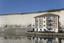 England, East Sussex, Brighton, apartment building in empty marina with chalk cliffs behind.