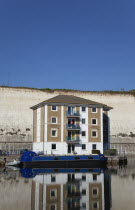 England, East Sussex, Brighton, apartment building in marina with moored barge and chalk cliffs behind.