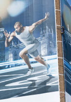 England, London, Stratford, A man suspended by rope secures giant hoarding of Gymnast, Louis Smith, to a building near train station.