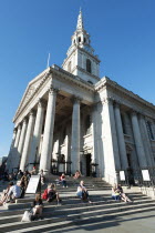 England, London, Trafalgar Square, tourists sat on the steps of St Martin in the Fields Church.