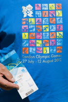 Sport, Olympic Games, London,  A spectator wearing an official T-shirt holding their official ticket for a Swimming session in the Aquatic Centre in the Olympic Park.