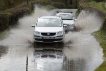 Weather, Floods, Flooded country road with cars driving slowly through waters.