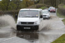 Weather, Floods, Flooded country road with cars driving slowly through waters.