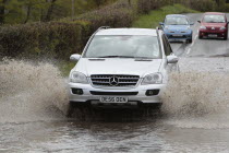 Weather, Floods, Flooded country road with cars driving slowly through waters.