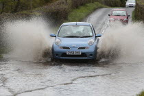 Weather, Floods, Flooded country road with cars driving slowly through waters.