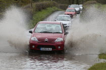 Weather, Floods, Flooded country road with cars driving slowly through waters.