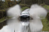 Weather, Floods, Flooded country road with cars driving slowly through waters.