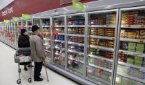 Food, Shopping, Supermarket, Elderly couple with shopping trolley looking at frozen goods in glass fronted freezer displays.
