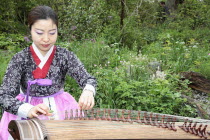 Music, Instrument, Stringed, Korean woman in traditional clothing playing Gayageum stringed instrument.