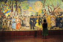 Mexico, Federal District, Mexico City, Visitor looking at Dream of a Sunday Afternoon in the Alameda, mural by Diego Rivera in the Museo Mural Diego Rivera.