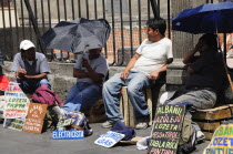 Mexico, Federal District, Mexico City, Workers plying trade outside the Cathedral in the Zocalo, using umbrellas for shade.