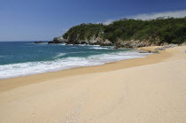 Mexico, Oaxaca, Huatulco,  Playa Conejos, Deserted beach with turquoise sea breaking on sandy shore and rocky headland.