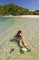 Mexico, Oaxaca, Huatulco, Snorkler adjusting mask while sitting in clear water beside Playa La Entrega.