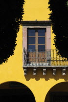 Mexico, Bajio, San Miguel de Allende, El Jardin, detail of yellow painted exterior facade of colonial mansion with French windows and balcony, part framed by silhouetted trees.