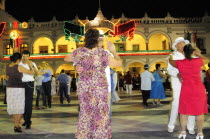 Mexico, Veracruz, Couples dancing in the Zocalo at night, illuminated decorations in the national colours for Independence Day celebrations on building facade behind.