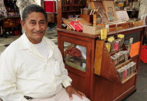 Mexico, Veracruz, Cigar seller in the Zocalo seated beside mobile stand with display of different cigars.