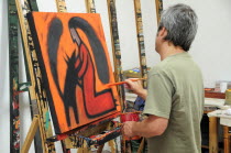 Mexico, Bajio, San Miguel de Allende, Artist Juan Ezcurdia in his studio working on painting at easel.