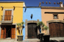 Mexico, Bajio, San Miguel de Allende, Colourful house facades on paved street with plant pots on roof balcony and outside wooden doors.