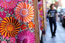 Mexico, Bajio, San Miguel de Allende, Brightly coloured embroidered textile hanging outside arts shop with flower design in pink, red and orange.