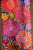 Mexico, Bajio, San Miguel de Allende, Detail of brightly coloured embroidered textile in arts shop with flower design in pink, red and orange.