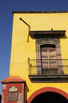 Mexico, Bajio, San Miguel de Allende, El Jardin, Part view of yellow painted exterior facade of building with French windows and balcony.