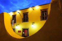 Mexico, Bajio, San Miguel de Allende, Half circle formed wall framing part view of opposite building at night with lighted lamps hanging from brackets at doorway.