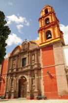 Mexico, Bajio, San Miguel de Allende. Exterior facade and bell tower of orange and yellow painted church building with flags hanging across doorway.