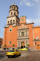 Mexico, Bajio, Queretaro, The church of San Francisco brightly coloured exterior facade with taxis and cyclist on road in foreground.
