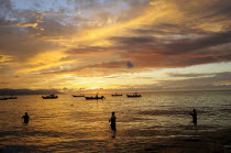 Mexico, Jalisco, Puerto Vallarta, Fishermen standing in sea with fishing boats at sunset.