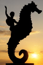 Mexico, Jalisco, Puerto Vallarta, Caballeo del Mar sculpture of boy riding a seahorse by Rafel Zamarripa silhouetted on the Malecon at sunset.