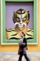 Mexico, Puebla, Young girl walking past poster of wrestler wearing mask and costume.