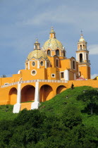 Mexico, Puebla, Cholula, Church of Neustra Senor de los Remedios or Our Lady of Remedios on wooded hillside above the pyramid ruins with brightly painted exterior in neoclassical style.