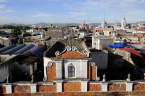 Mexico, Puebla, View across city rooftops with part view of red brick and white building facade in foreground.