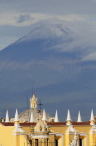 Mexico, Puebla, View of volcanic peak of Popocatepetl wreathed in cloud with Puebla rooftops in foreground.